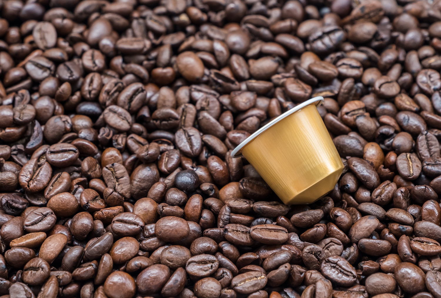 Gold coffee pod surrounded by roasted coffee beans