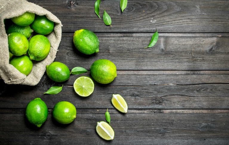 Fresh lime in the sack and pieces of juicy lime. On wooden background